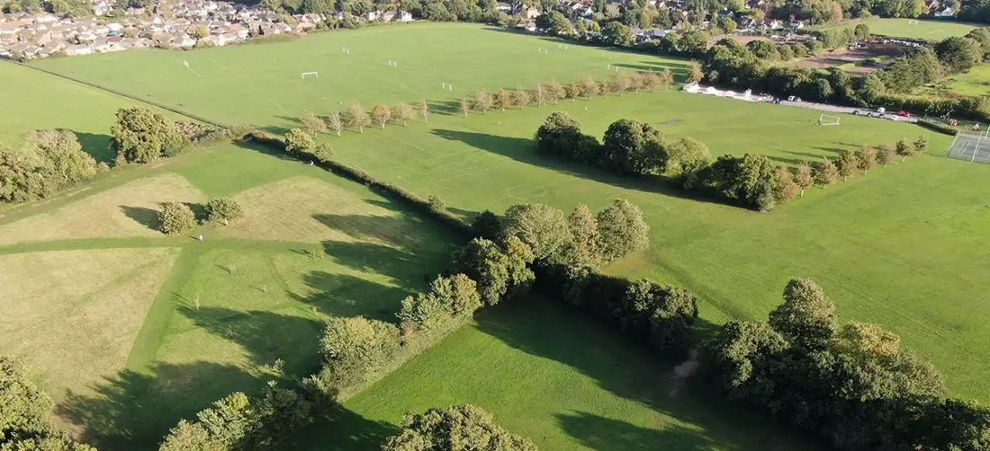 An aerial photograph of six pasture fields, each surrounded by mature farm hedgerows and there's a village in the background.